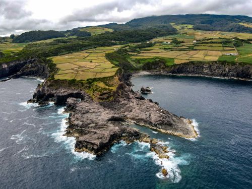 Free Aerial view of rugged coastal cliffs and lush farmland meeting the ocean under cloudy skies. Stock Photo