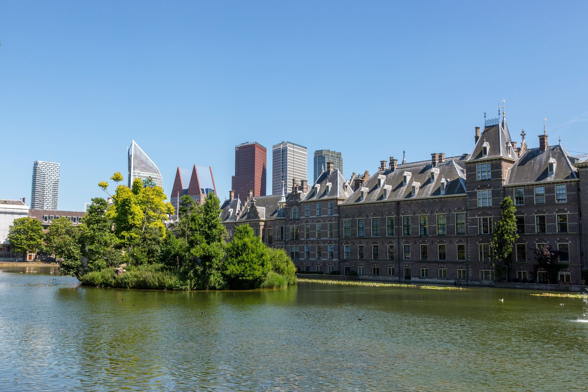 Prachtig uitzicht op het Binnenhof en de moderne skyline van Den Haag, weerspiegeld in de Hofvijver op een zonnige dag.