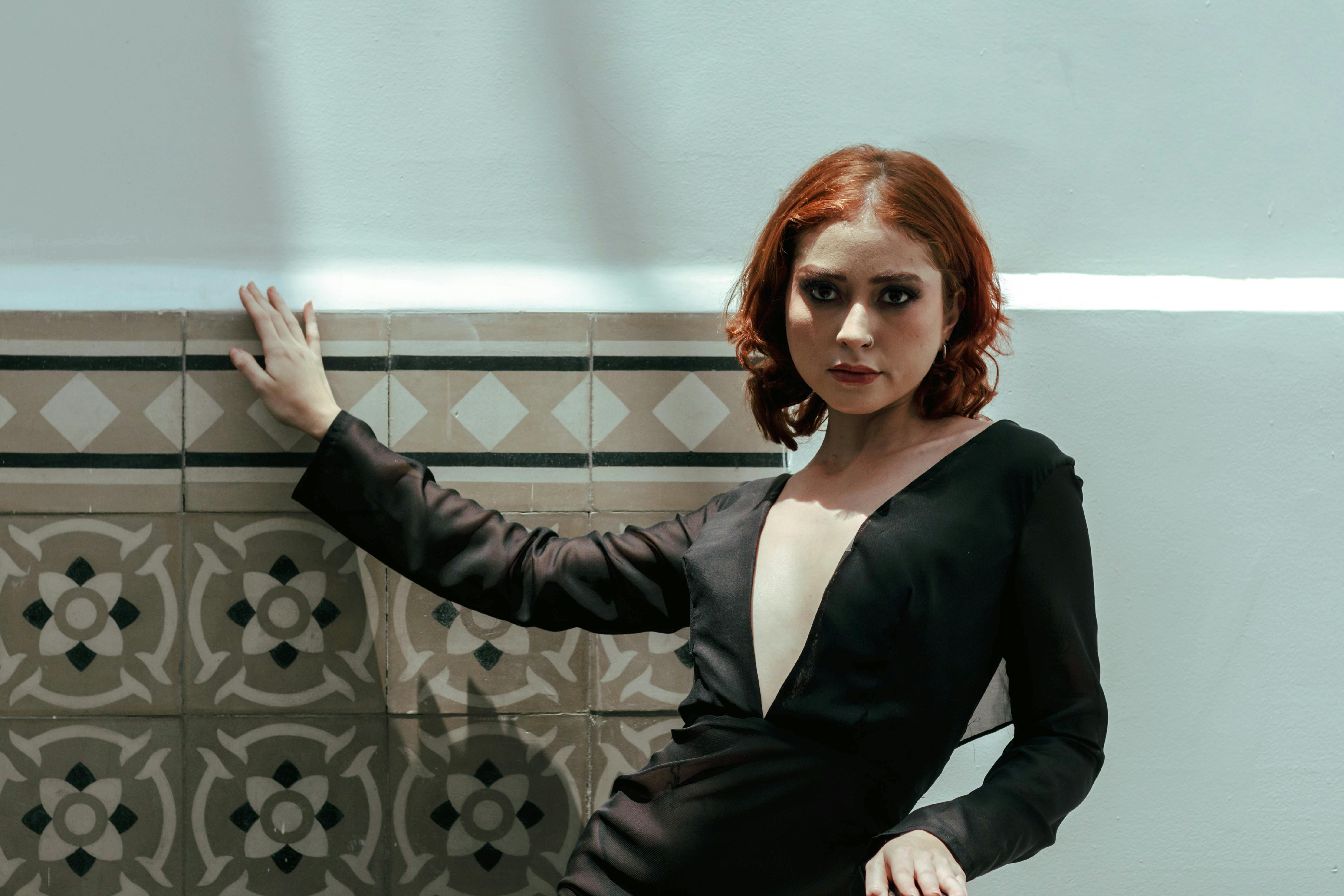 bezplatná Žena v elegantních černých šatech pózuje u vzorované zdi a vyzařuje eleganci. Základová fotografie