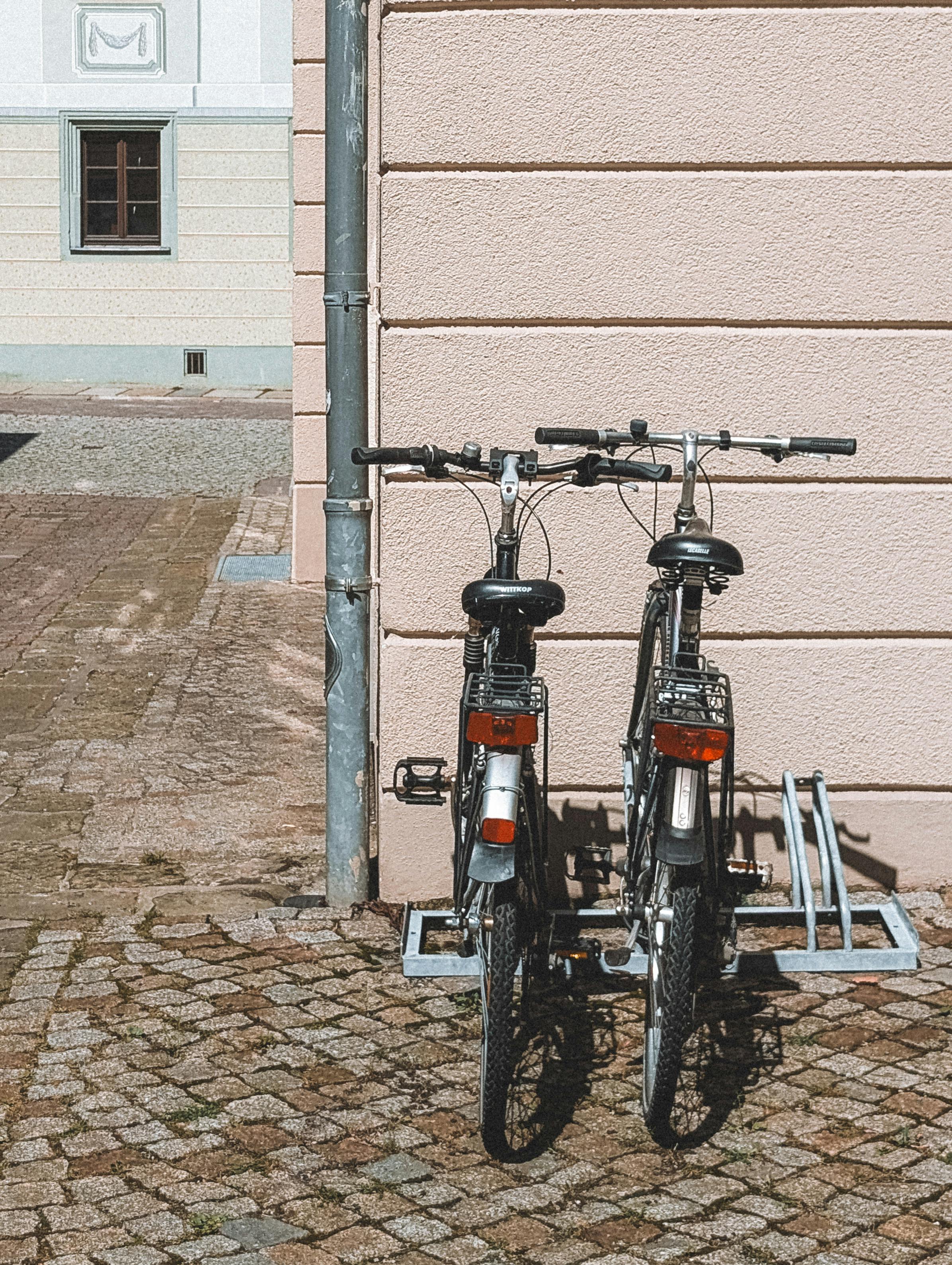 Two bicycles parked against a beige wall in sunny Pirna, Germany street.