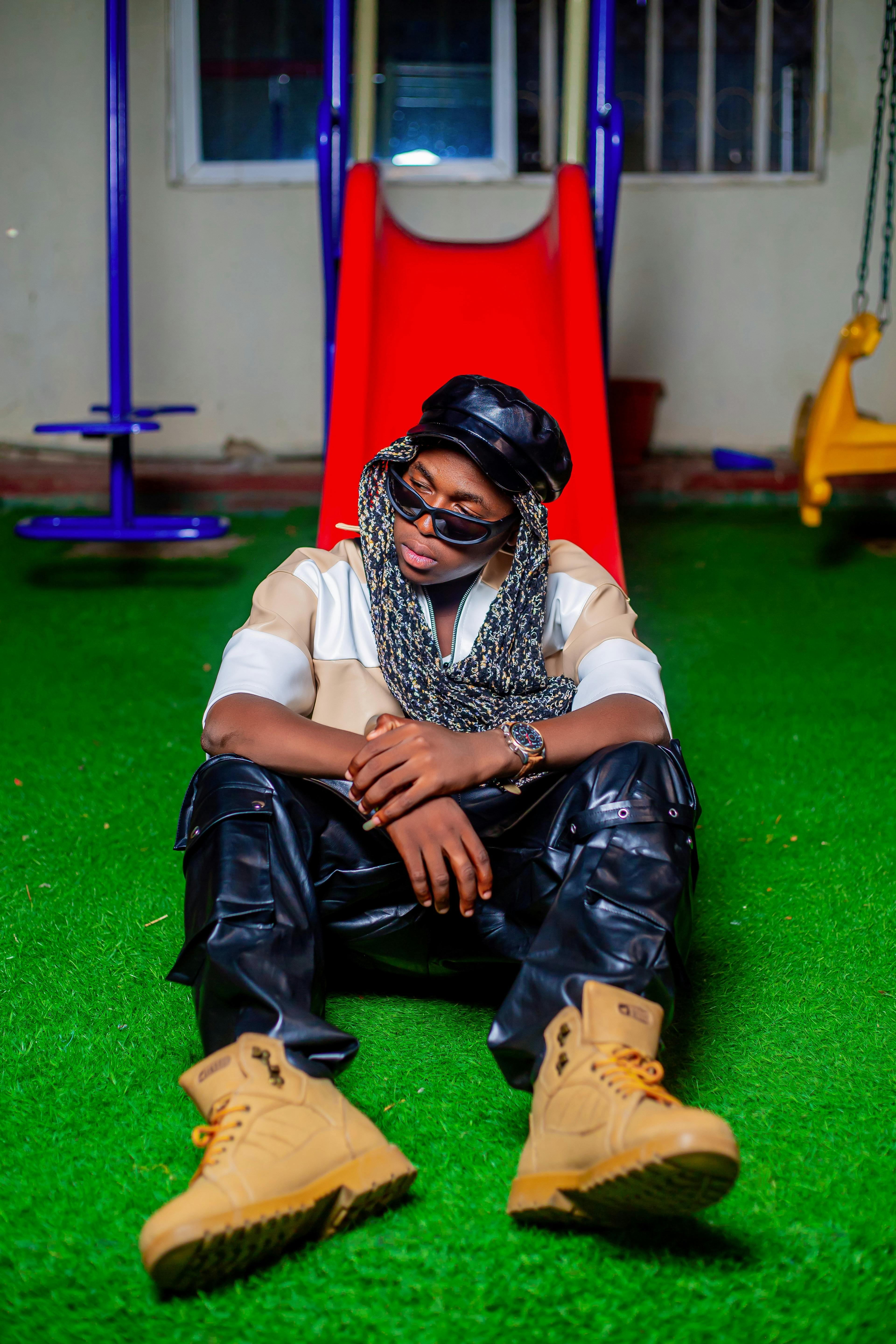 Young man in trendy fashion sits at playground slide showcasing modern urban style.