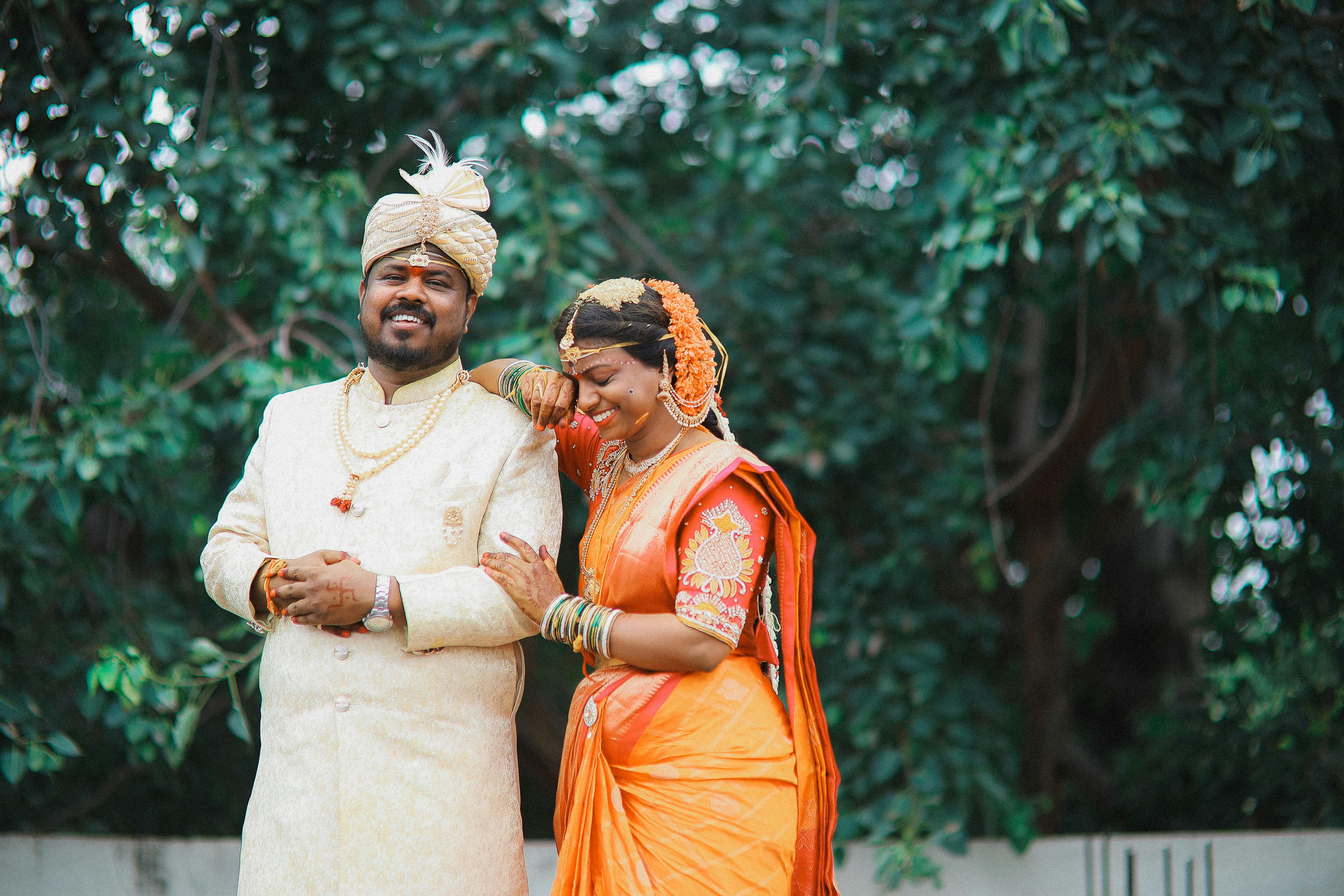 A happy South Asian couple in traditional attire enjoying their wedding day outdoors.