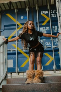 Stylish woman poses confidently in urban setting with industrial container backdrop.