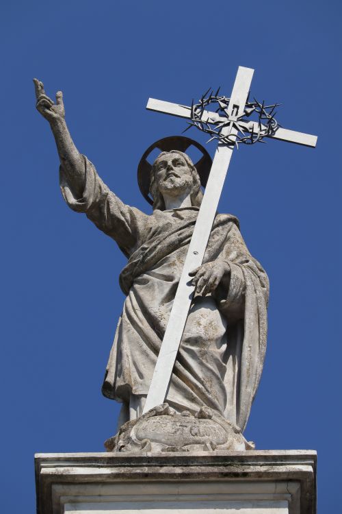 Free A striking statue of Christ holding a cross against a clear blue sky, symbolizing faith and devotion. Stock Photo