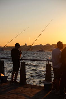 Fishermen casting lines against a stunning İstanbul sunset with city skyline in view.
