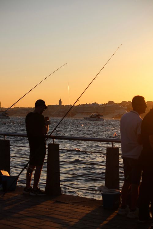 Free Fishermen casting lines against a stunning İstanbul sunset with city skyline in view. Stock Photo