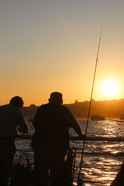 Free Silhouette of fishermen casting rods against a vibrant sunset on Istanbul's Bosphorus. Stock Photo