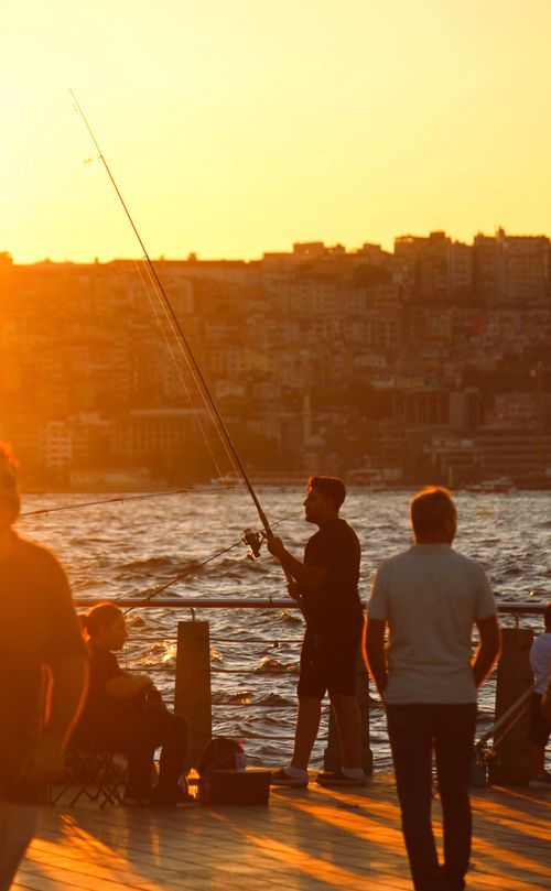 Free Silhouetted fishermen casting lines against a golden sunset over the Bosphorus in Istanbul. Stock Photo