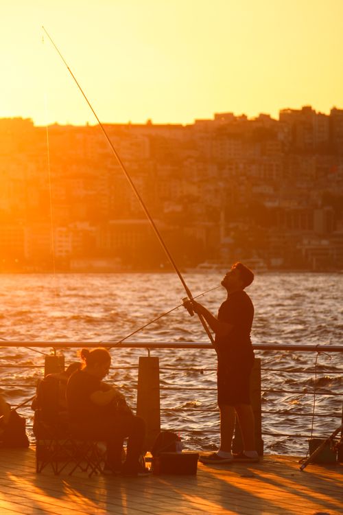 Free A fisherman casts his line at sunset in Istanbul, creating a serene silhouette against the glowing skyline. Stock Photo