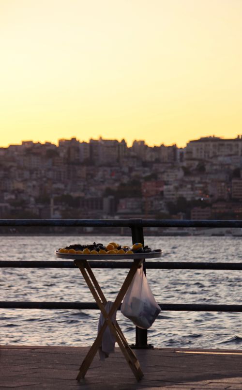 Free Serene sunset over a city skyline by the waterfront, featuring a small snack stand in the foreground. Stock Photo