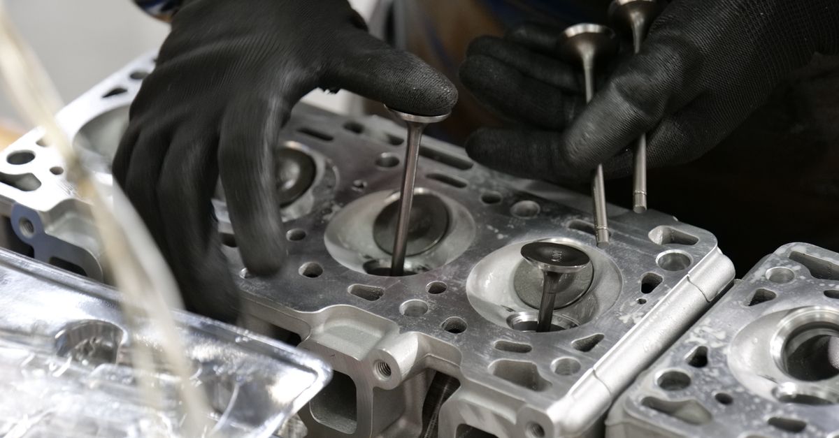 Close-up of mechanic's hands working on engine cylinder head assembly with valves.