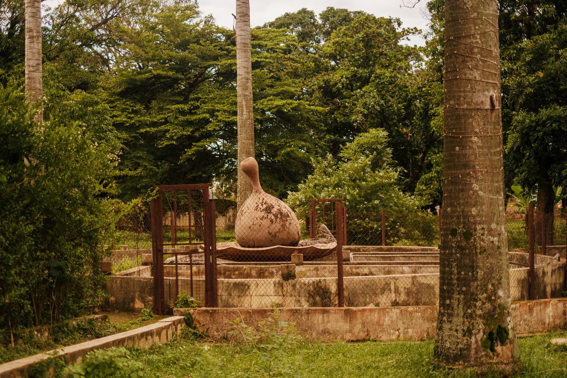 A serene outdoor sculpture in Kaduna, Nigeria, amidst lush green trees and grass.