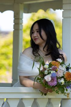Bride holding colorful bouquet in a gazebo during summer in Sweden.