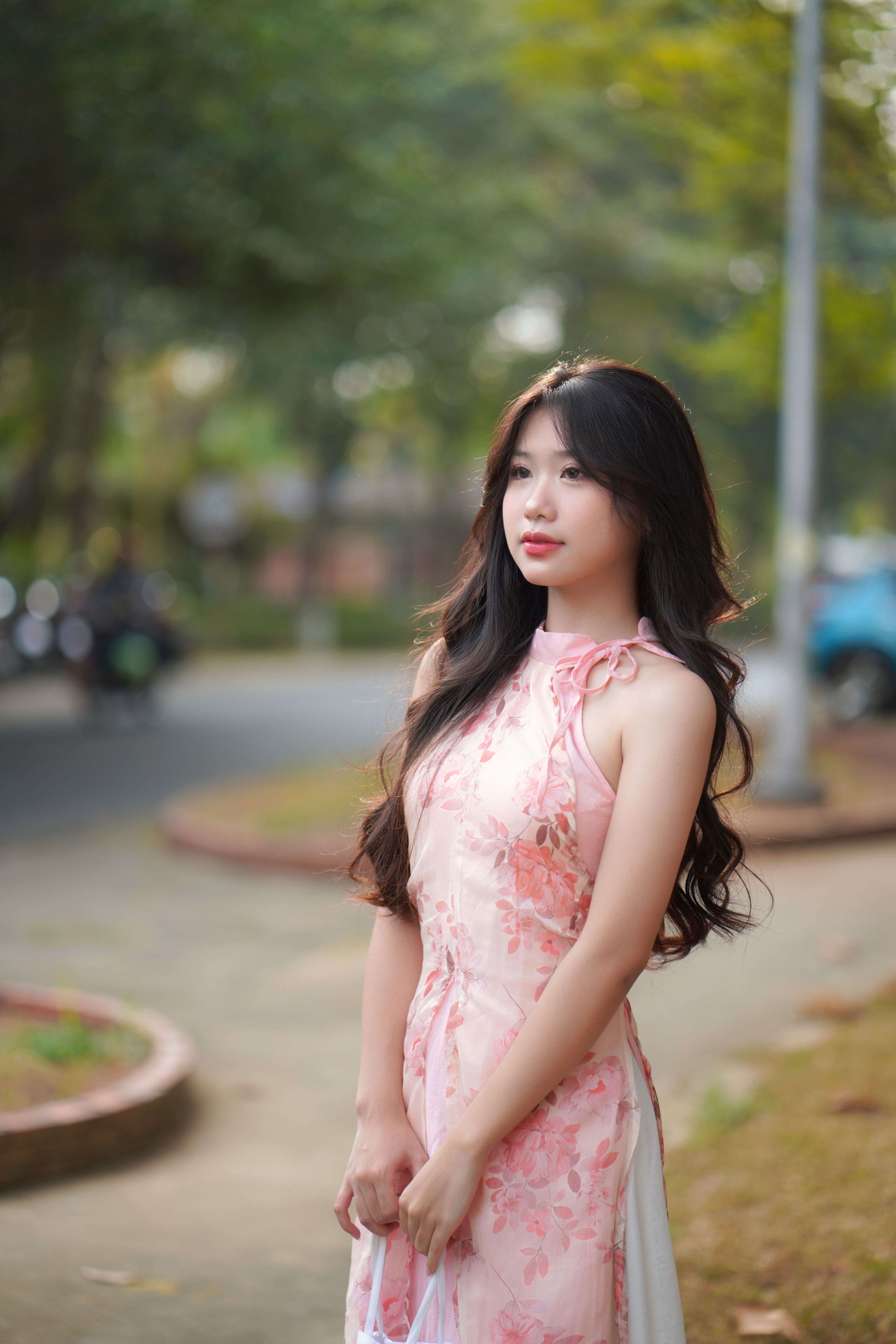 A young woman wearing a pink floral dress poses gracefully outdoors with a serene expression.