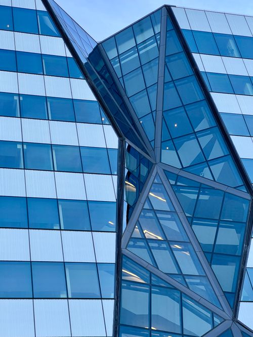 Free Close-up of a modern geometric glass facade with reflective blue windows. Stock Photo