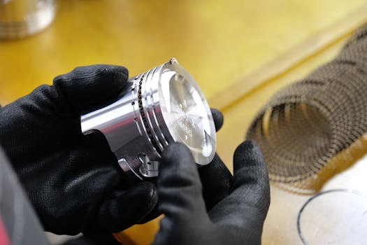Close-up of black-gloved hands examining a metal engine piston in a workshop.