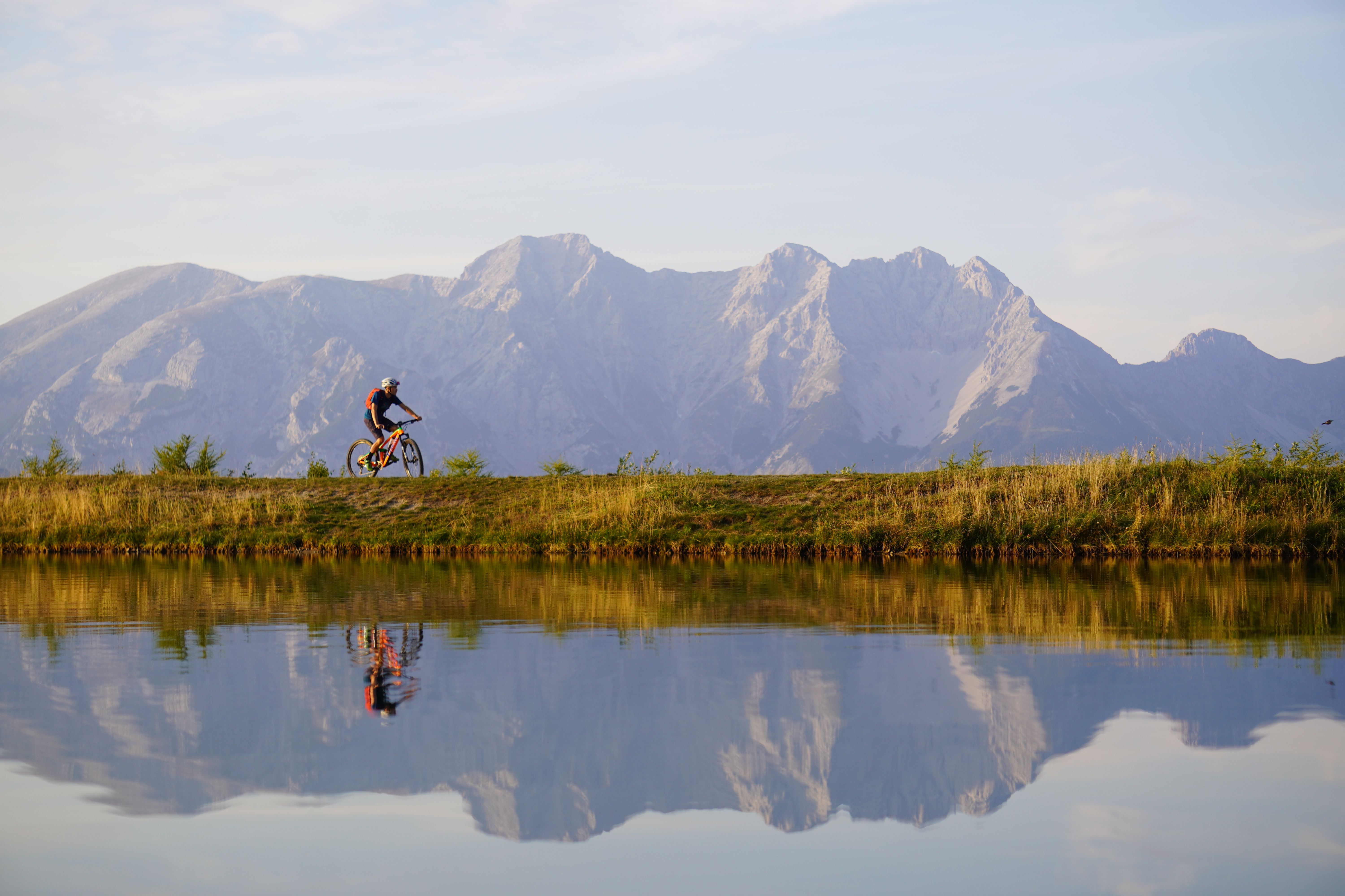 A mountain biker rides along a scenic lake with majestic mountain views in Tirol, Austria.