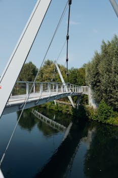A contemporary footbridge crossing a serene river surrounded by lush greenery in France.