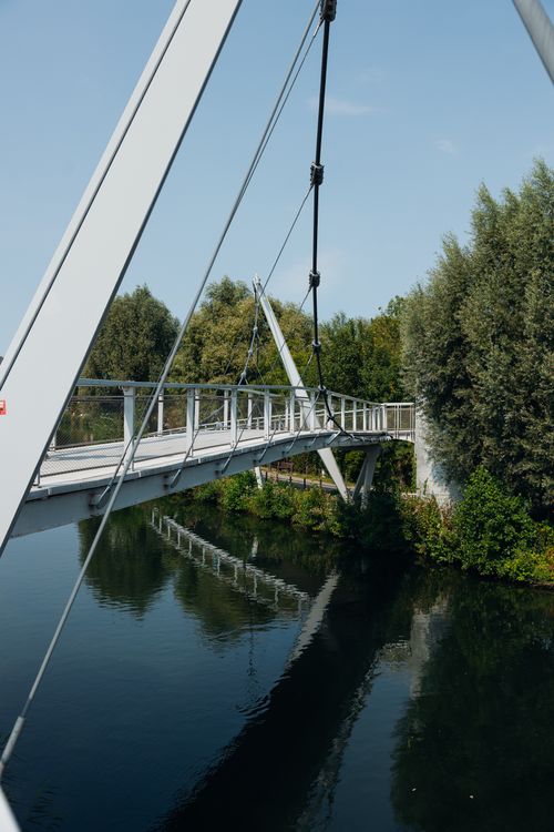 Free A contemporary footbridge crossing a serene river surrounded by lush greenery in France. Stock Photo