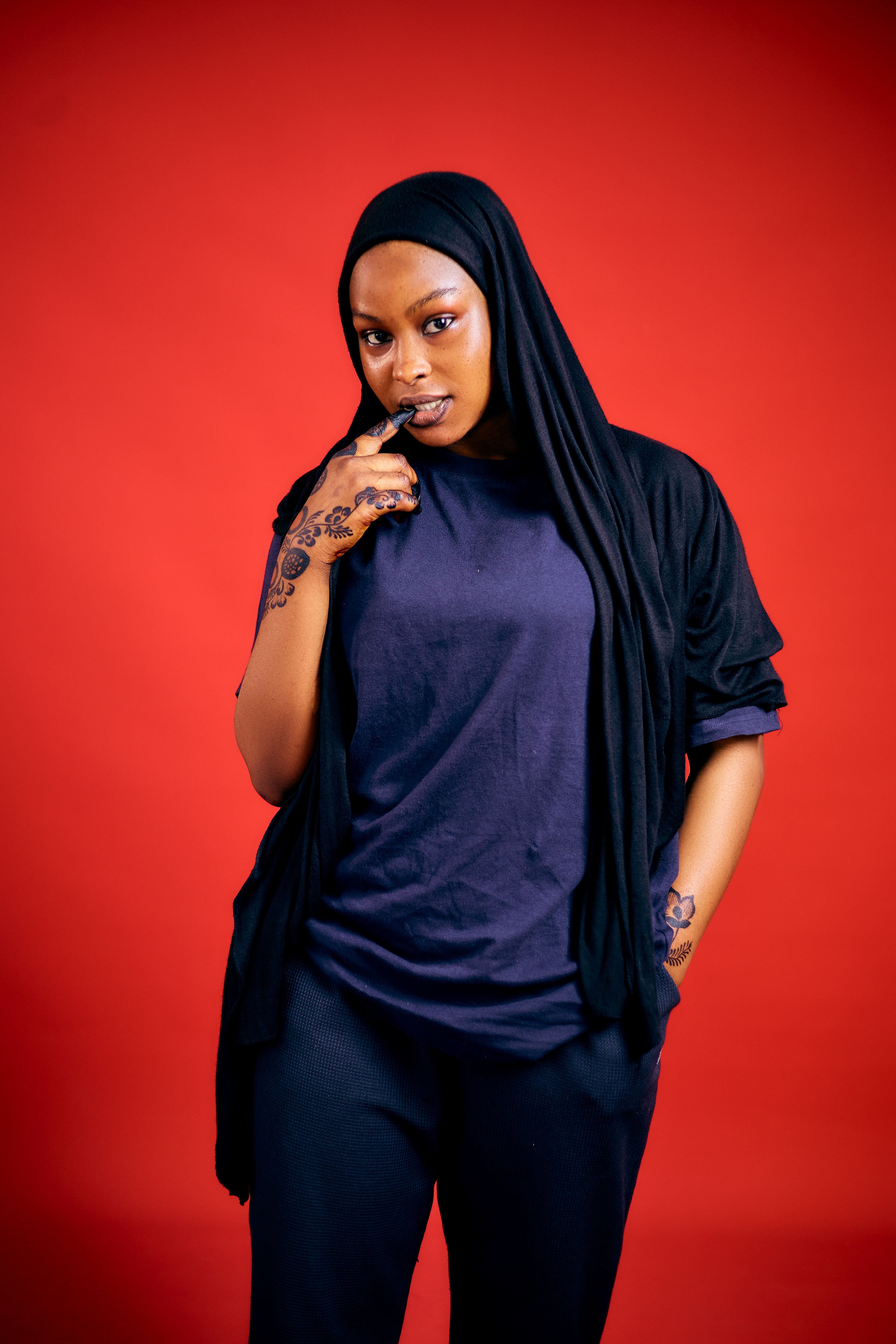 Portrait of a woman in a hijab with intricate henna art, set against a bold red background.