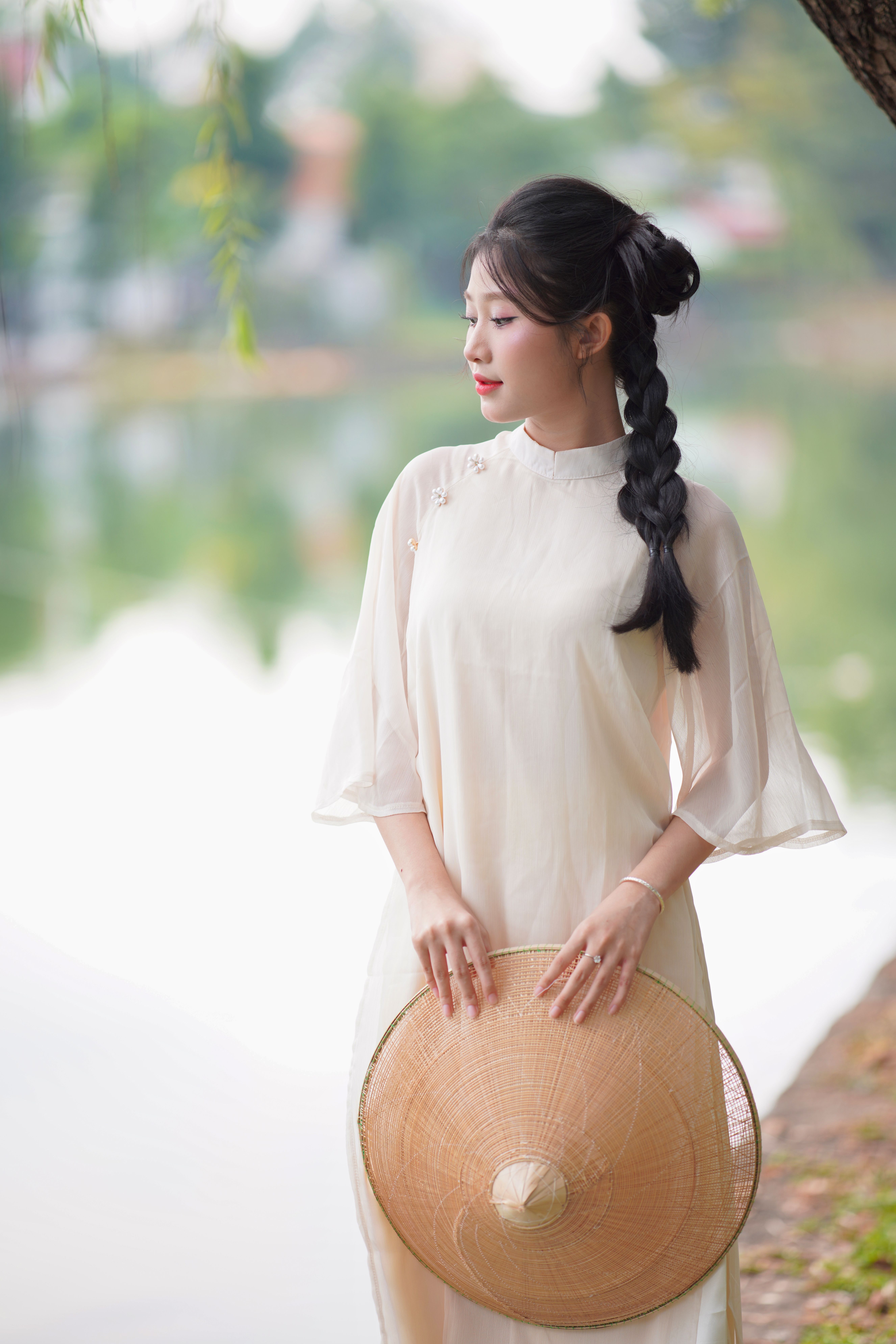 Beautiful woman with braided hair holding a straw hat by a scenic lake.