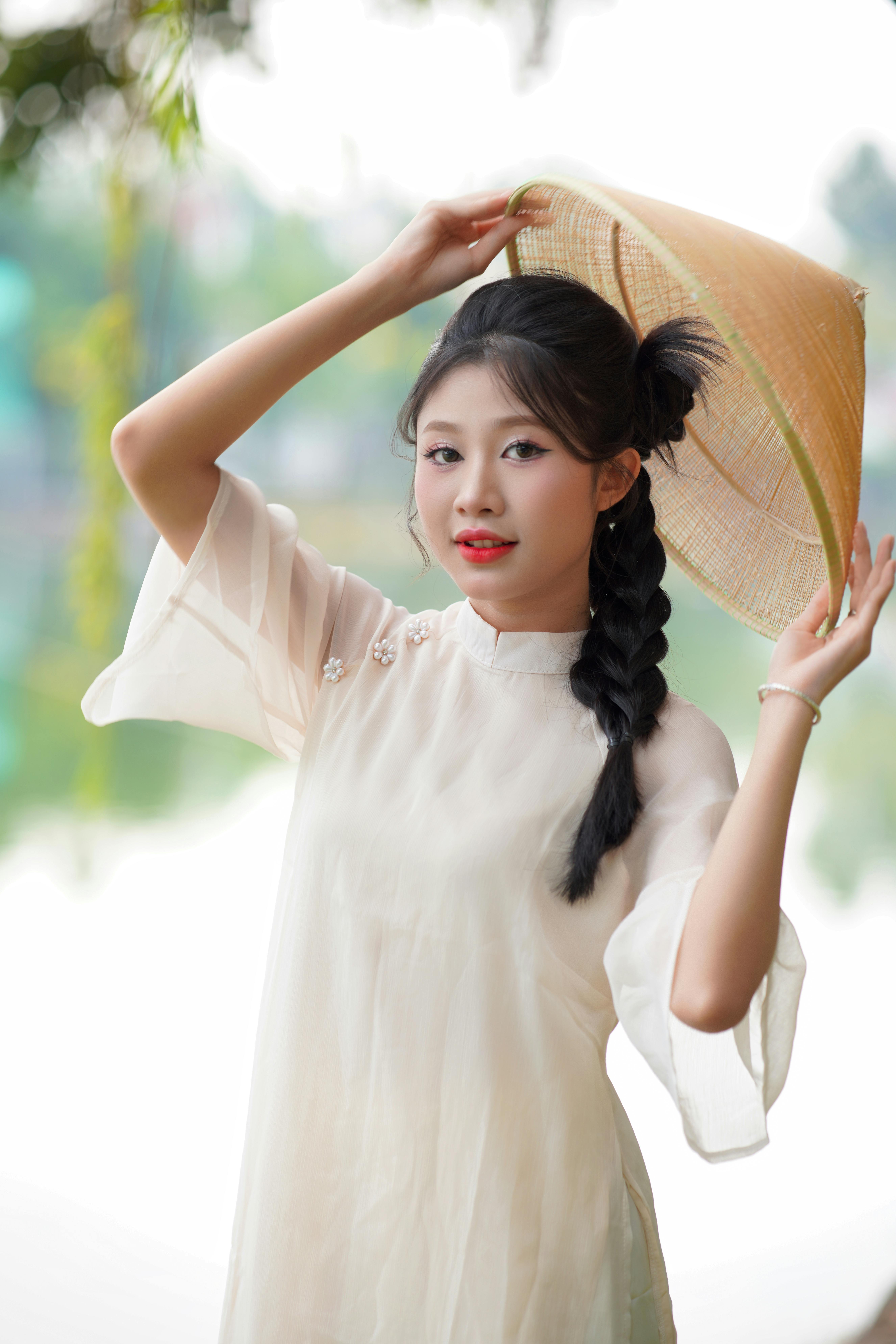 Portrait of a young woman wearing an ao dai and conical hat outdoors.