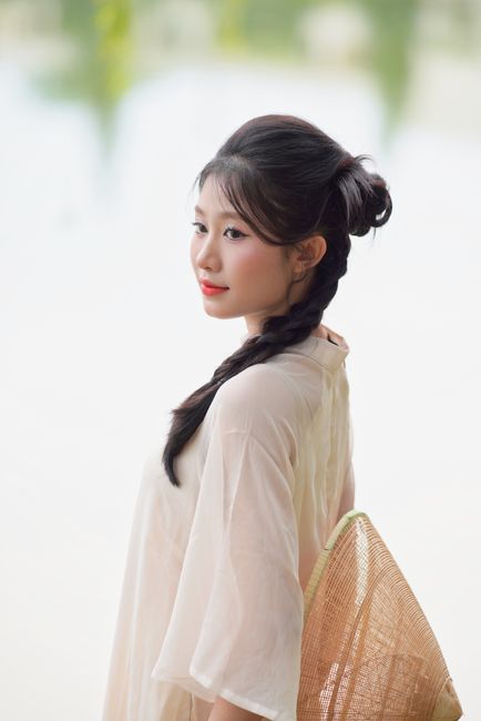 A serene portrait of a woman in a white dress with braided hair, outdoors.