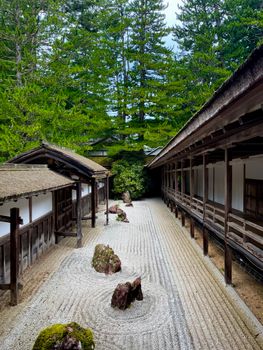 A tranquil Japanese Zen garden surrounded by traditional wooden architecture and lush greenery.