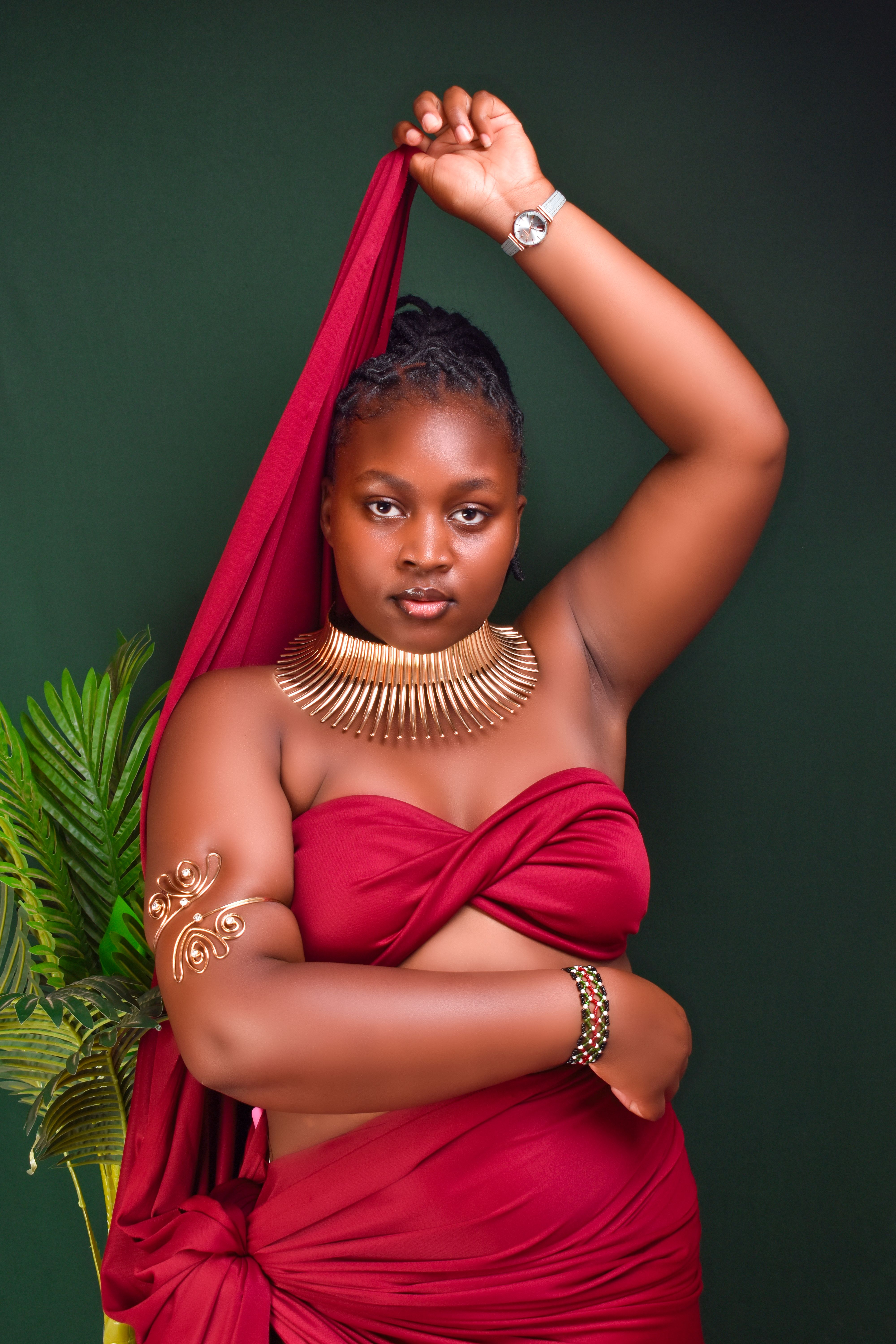 Striking portrait of a woman wearing red fabric, jewelry, and a watch against a dark green background.