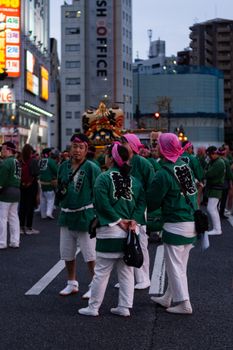 Group of people in green attire during a Japanese street festival in city setting at dusk.