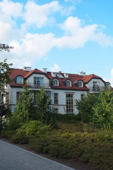 A picturesque red roof mansion surrounded by lush greenery, captured on a sunny day.