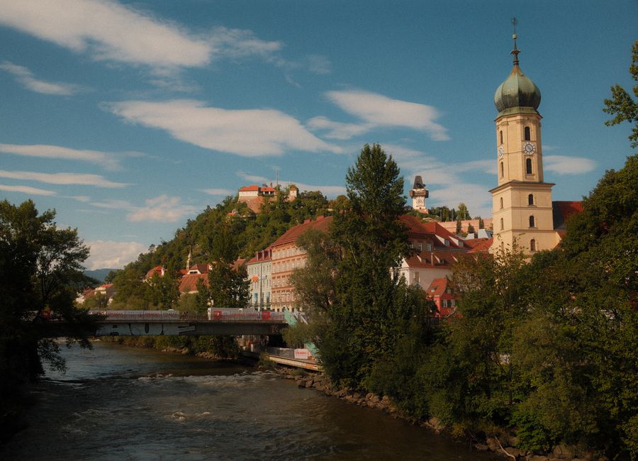 Picturesque landscape of Graz, Austria featuring the historic Uhrturm and cascading river under a bright sky.