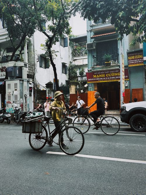 Free A vibrant street scene in Hanoi featuring cyclists and local vendors amidst urban life. Stock Photo
