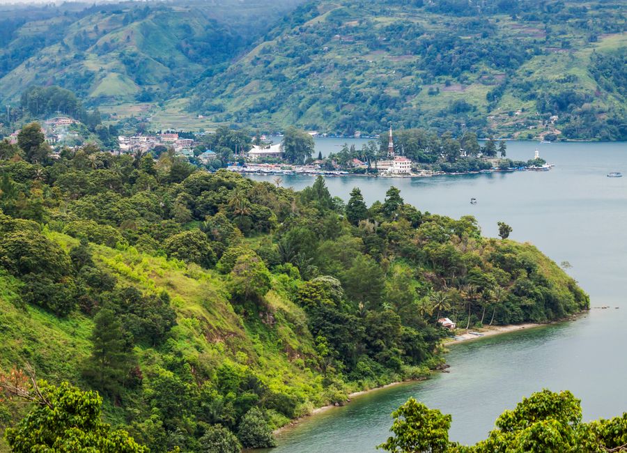 Lush green hills overlooking a serene lake with a distant village. Perfect for travel and nature enthusiasts.