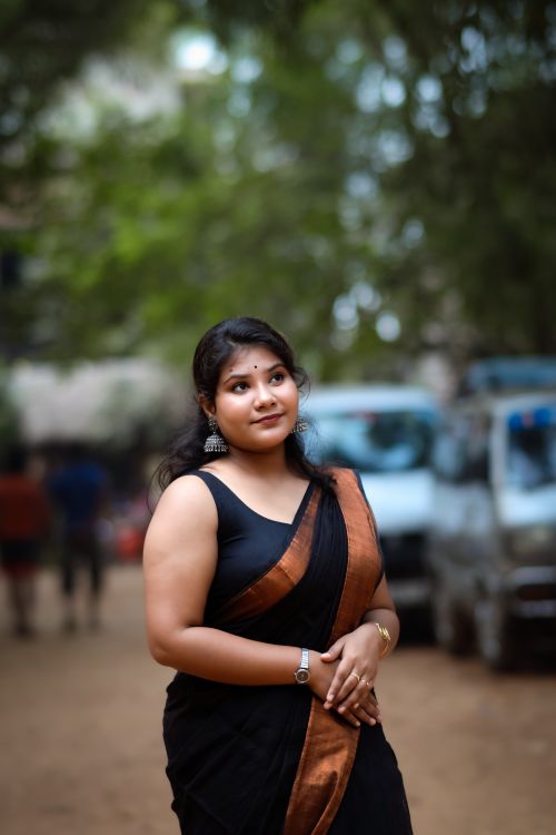 Free Portrait of a woman in a black sari with brown border, outdoors with soft focus background. Stock Photo