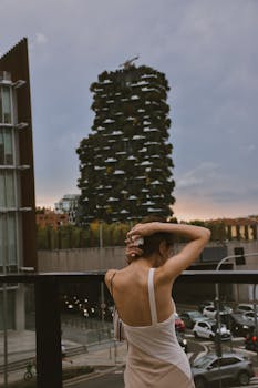 A fashionable woman gazes at the Bosco Verticale skyscraper in Milan during sunset.