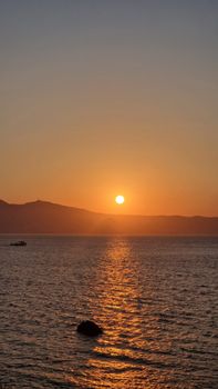 Captivating sunset over a calm ocean with distant hills silhouette, creating a tranquil and warm ambiance.