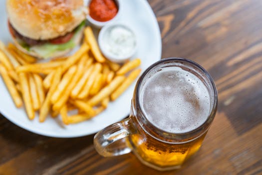 A mouth-watering hamburger served with fries, accompanied by a glass of beer on a wooden table.