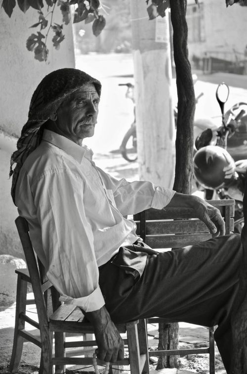 Free Black and white portrait of an elderly man sitting outdoors in a village, exuding a calm and reflective vibe. Stock Photo