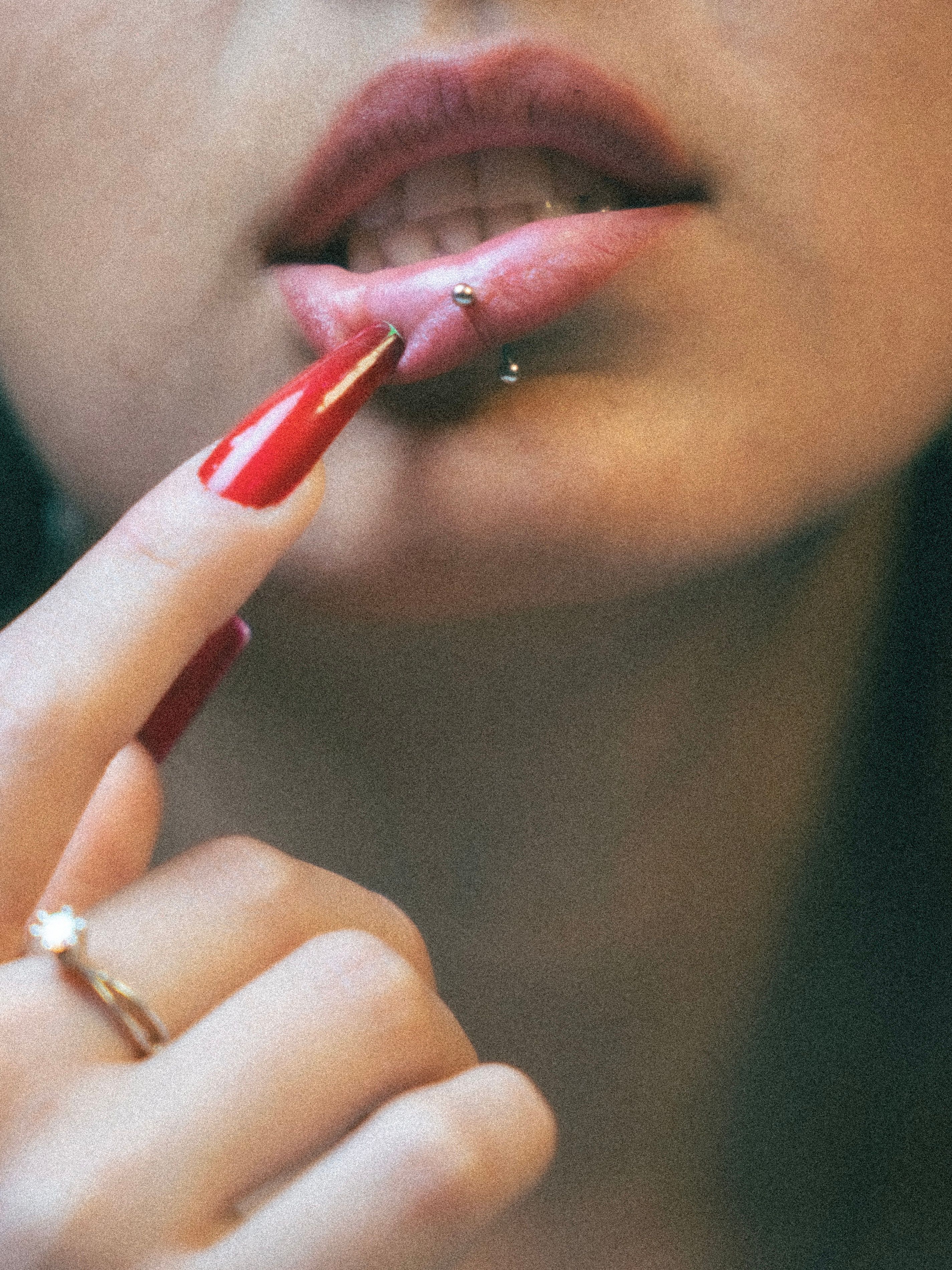 Fotomural Acercamiento artístico de labios perforados y manicura roja, capturando estilo moderno.