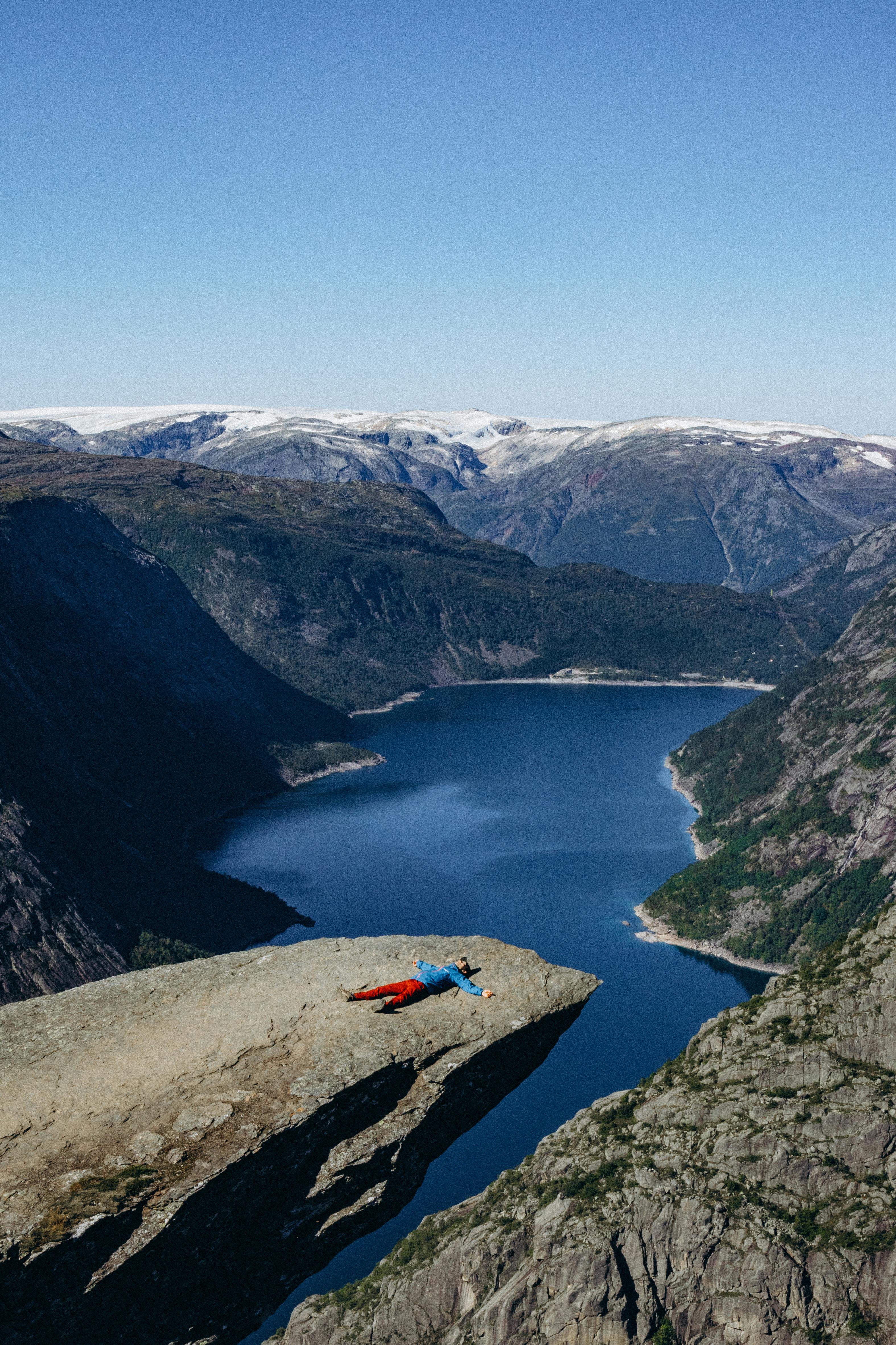A person lies on Trolltunga cliff overlooking the stunning fjords in Vestland, Norway.