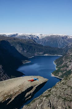 A person lies on Trolltunga cliff overlooking the stunning fjords in Vestland, Norway.