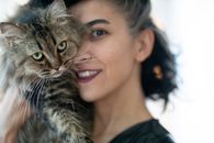 室内，一个女人正亲切地抱着一只蓬松的虎斑猫