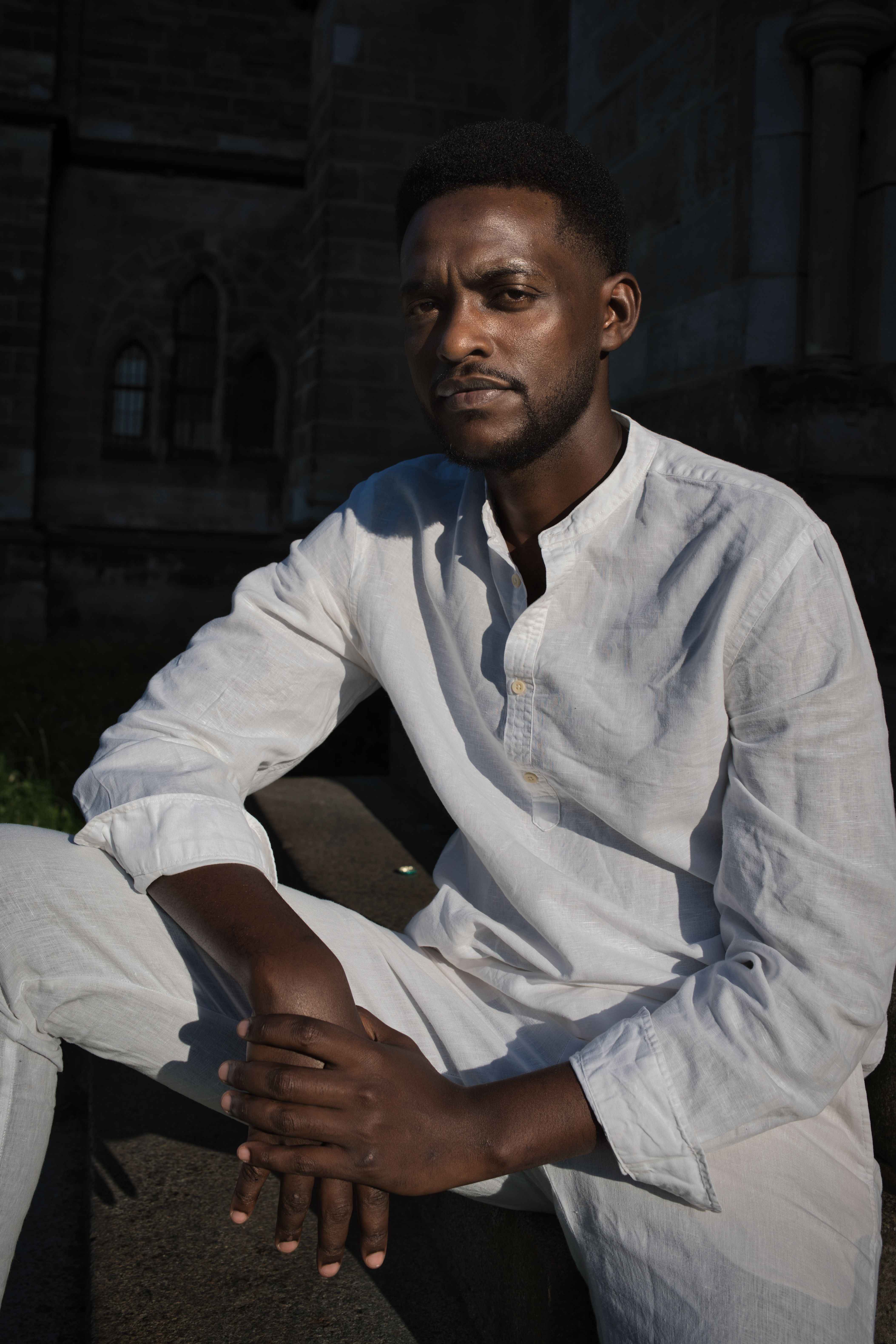 A contemplative man in white attire sits near historic Berlin architecture, captured in natural light.