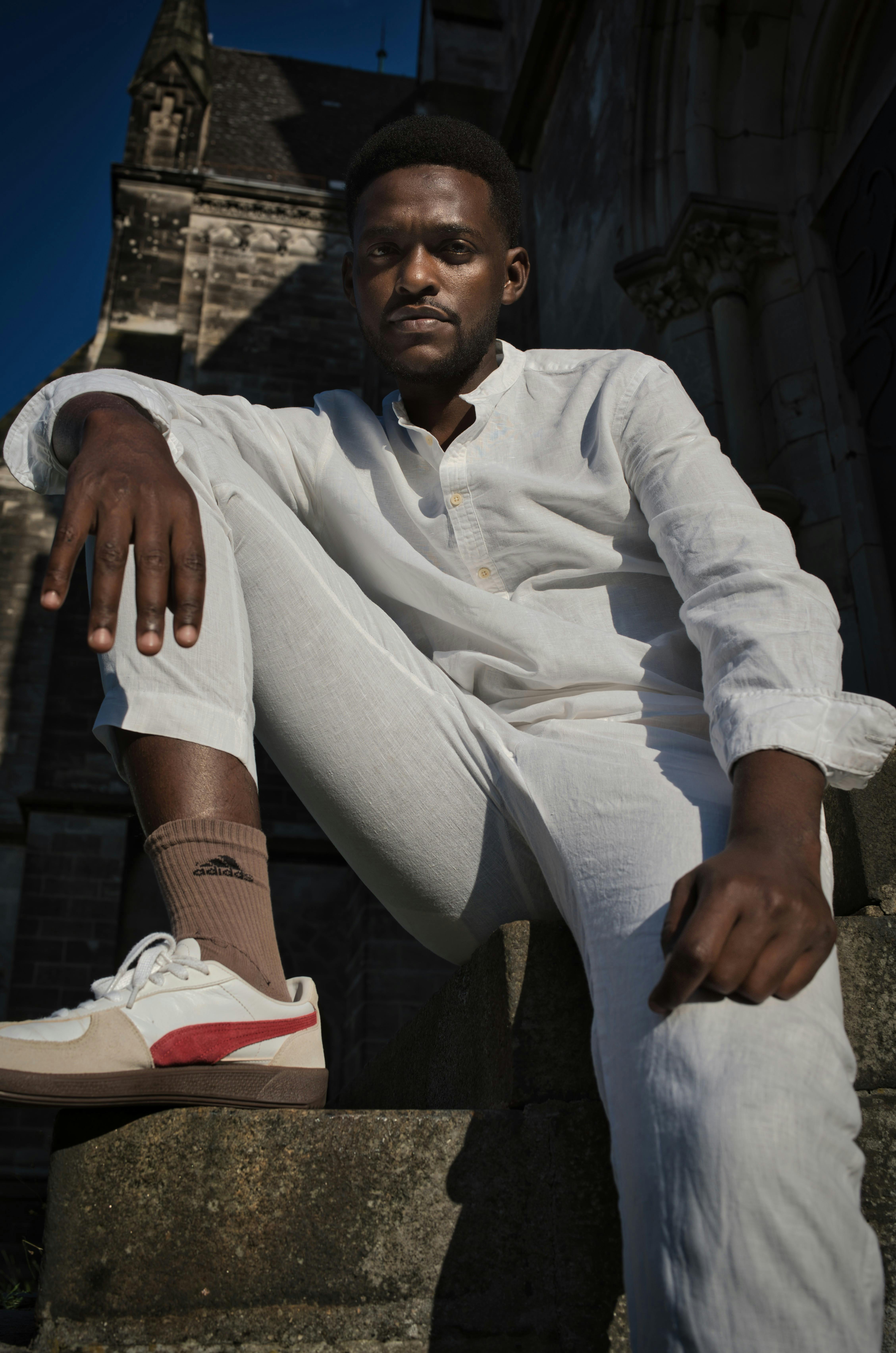 Confident male model in white attire posing outdoors in Berlin's architectural landscape.