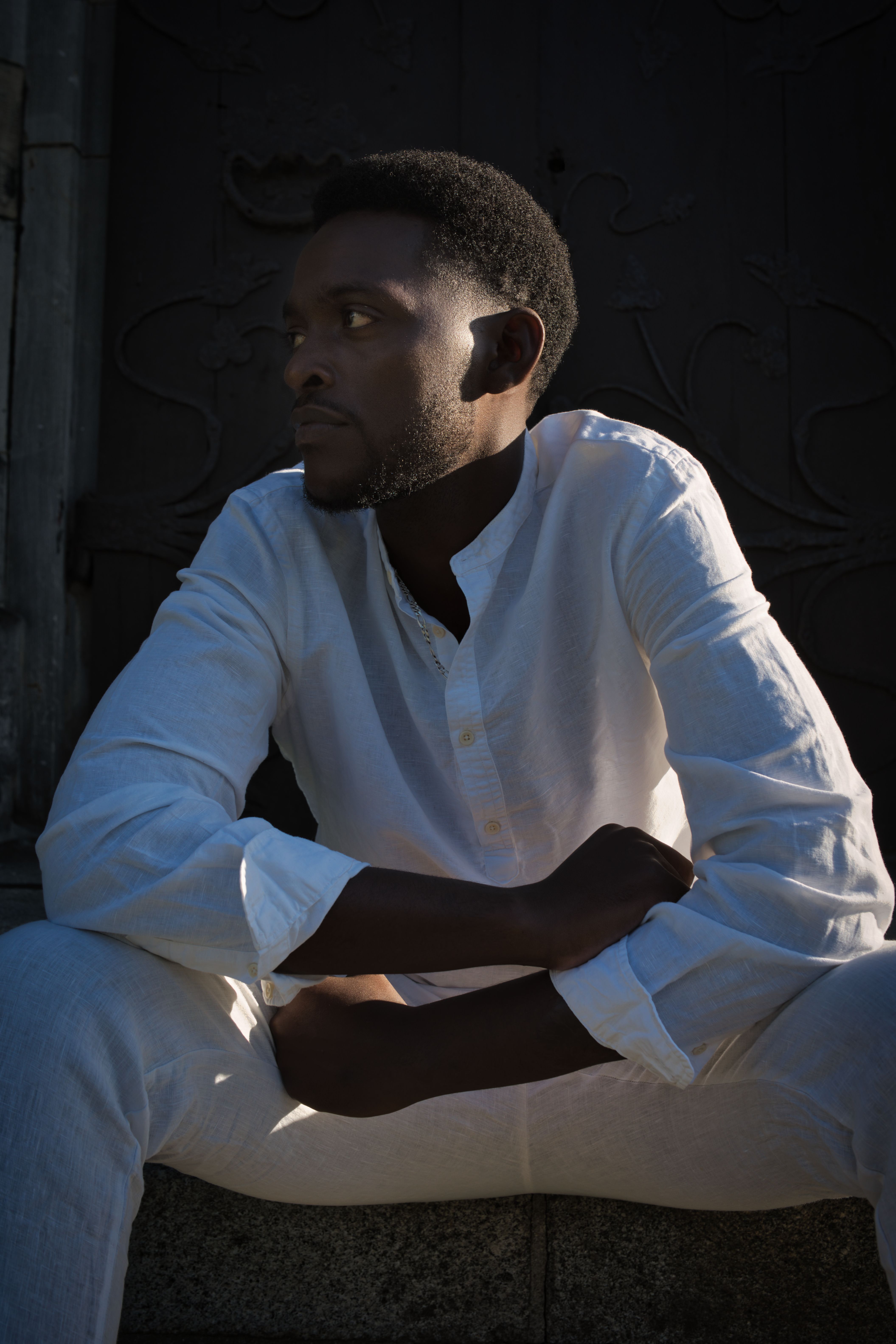 Portrait of a man in white attire sitting in Berlin, exuding a thoughtful and serene mood.