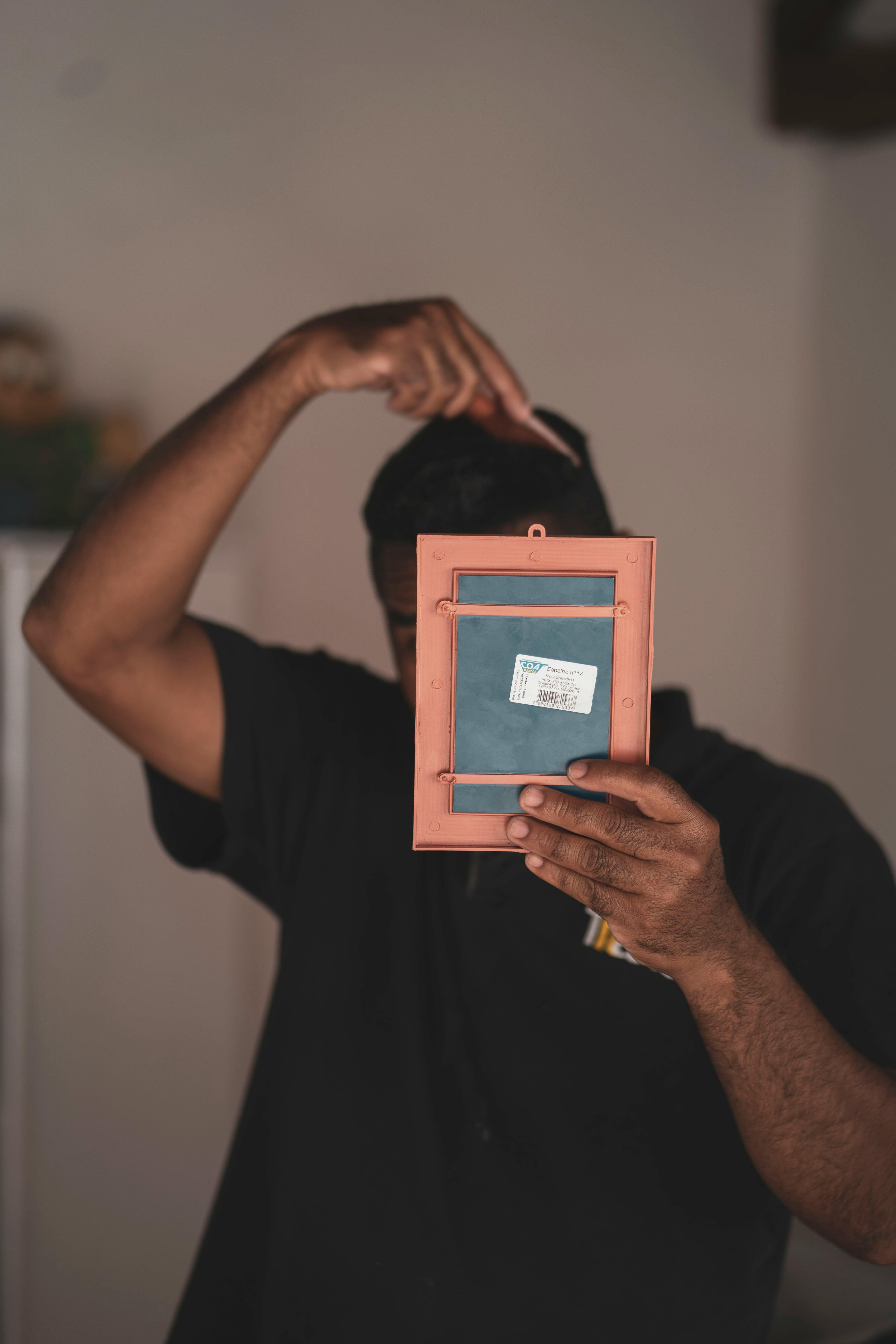 Gratis Un uomo tiene in mano una cornice vuota mentre si pettina, creando un momento giocoso e spontaneo. Foto a disposizione