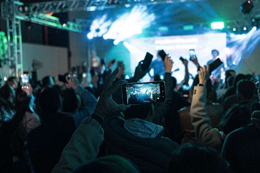 A concert crowd holding up smartphones with bright lights at a live show