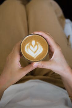 Close-up view of a person holding a cup of latte with intricate coffee art, showcasing a serene and cozy moment.
