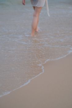 Person walking along calm beach shore, capturing serene summer vibes.